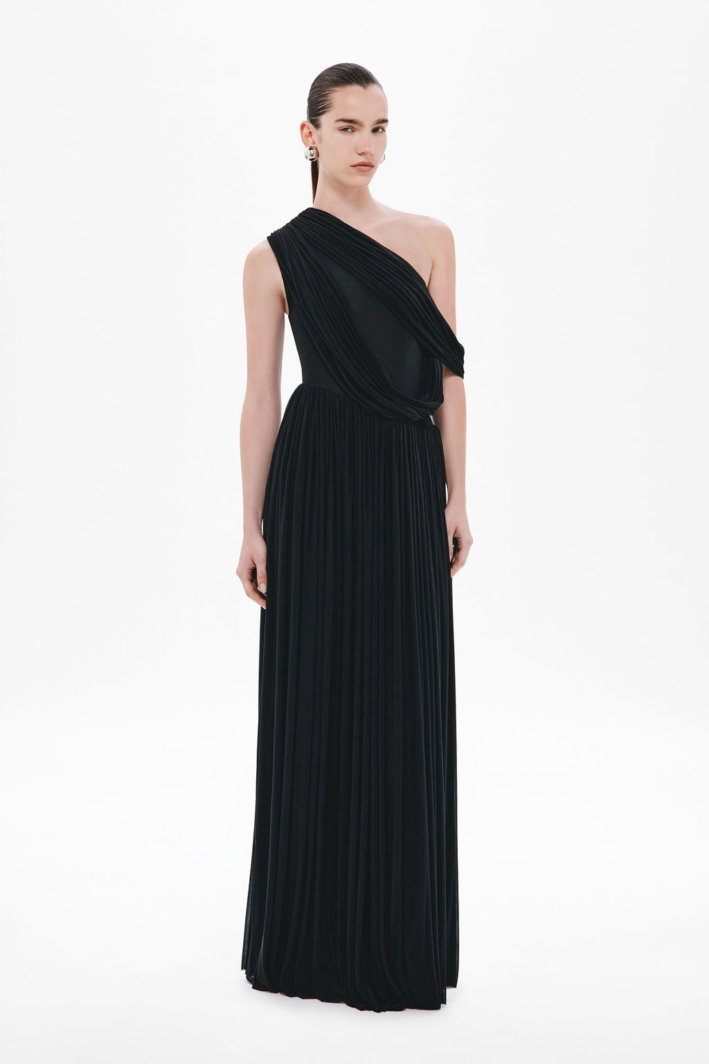 Black one-shoulder maxi stocking dress with draped diagonal strap and pleated skirt