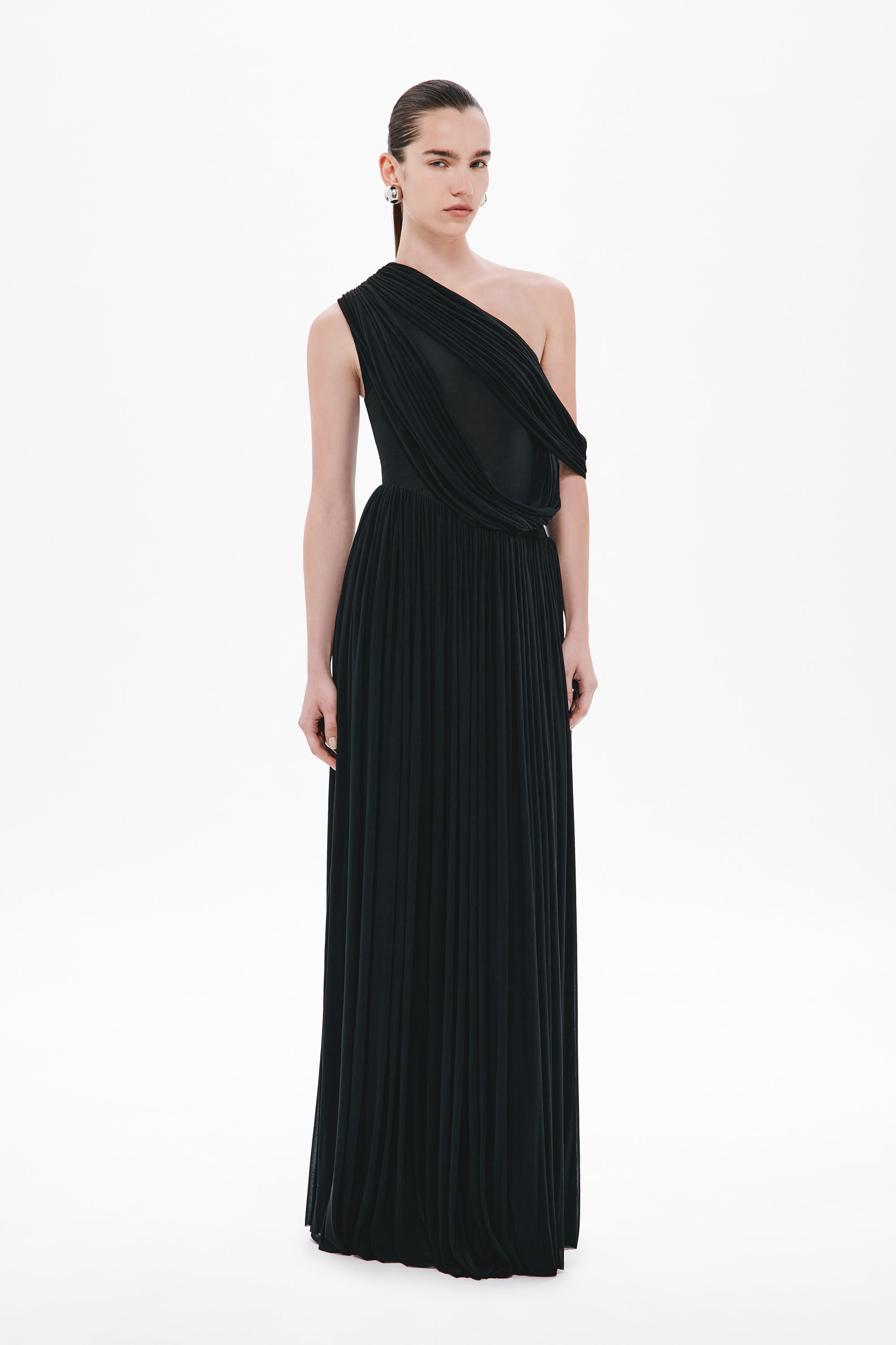 Black one-shoulder maxi stocking dress with draped diagonal strap and pleated skirt