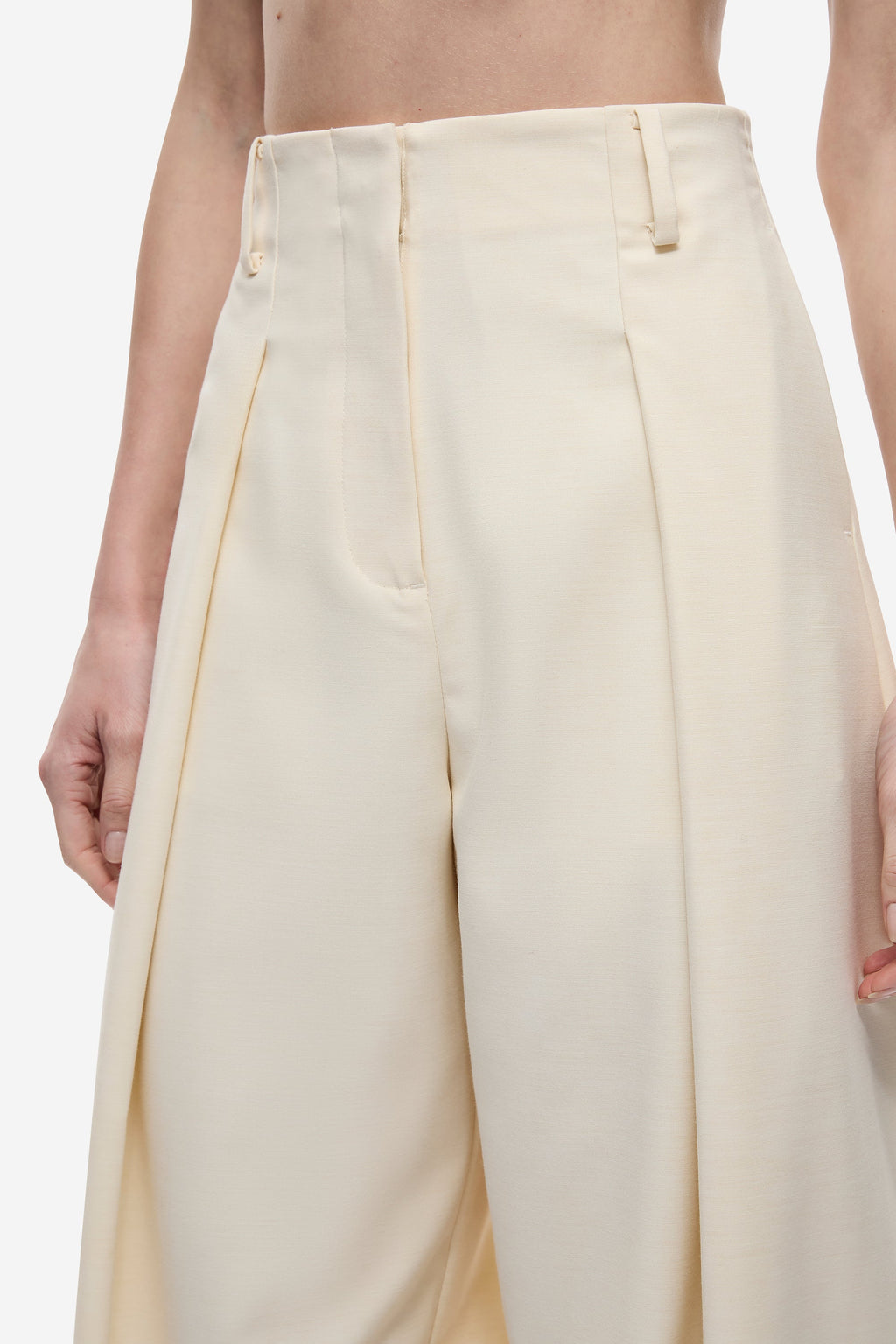 Cream high-waist trousers close-up with pleats, belt loops, and front closure