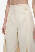 Cream high-waist trousers close-up with pleats, belt loops, and front closure