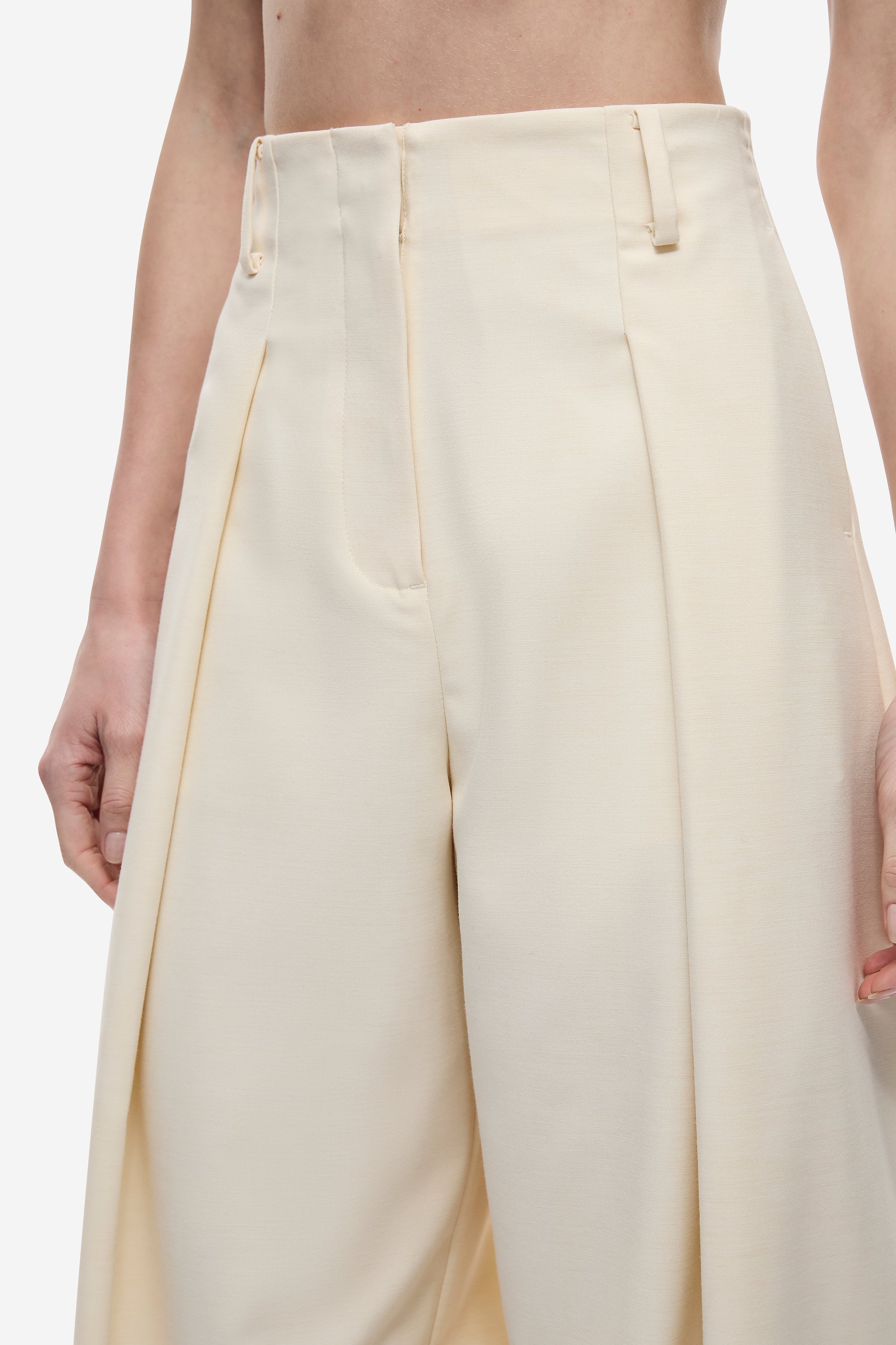 Cream high-waist trousers close-up with pleats, belt loops, and front closure