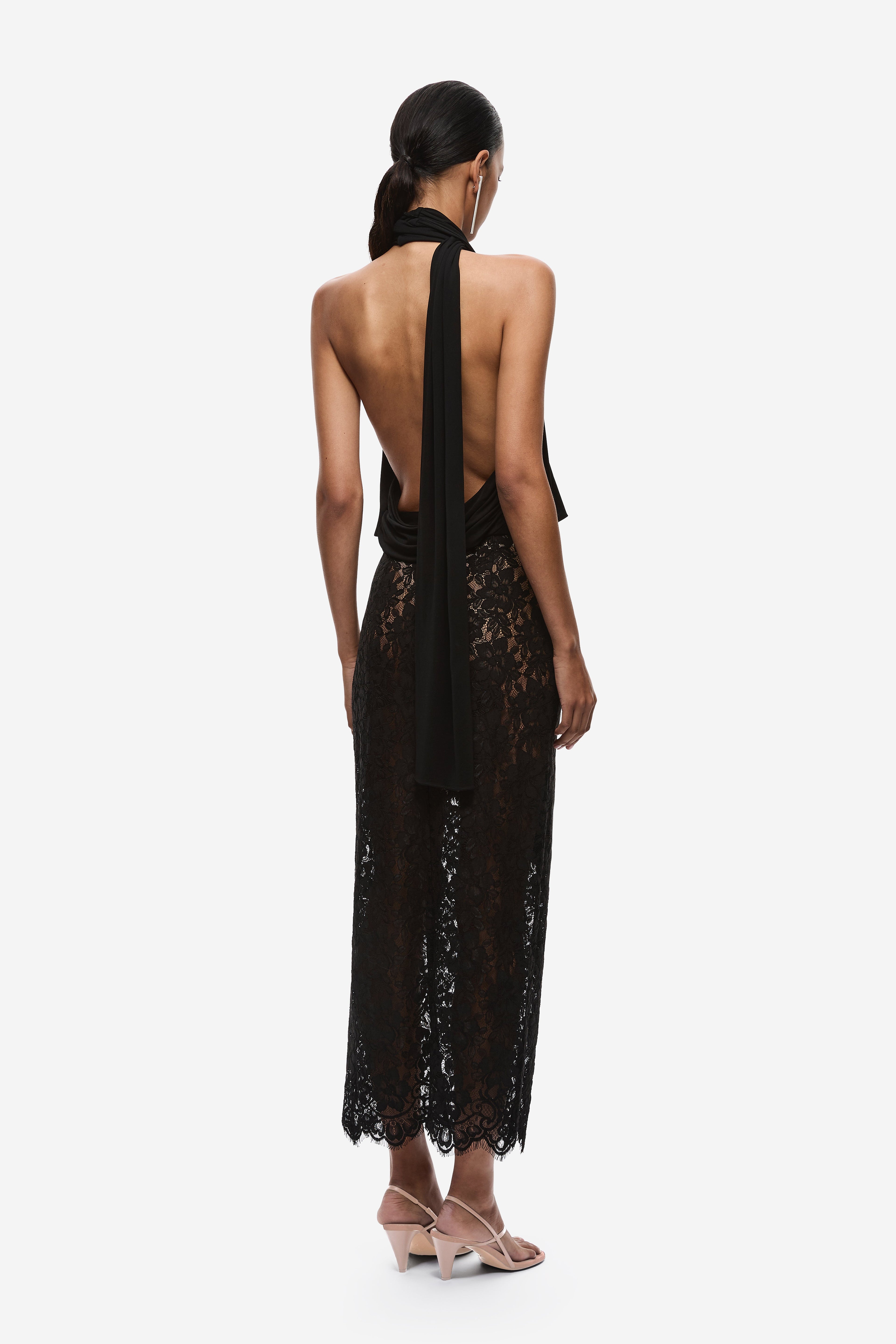 Black halter jersey top with open back, draped sash tie, and lace hem panel