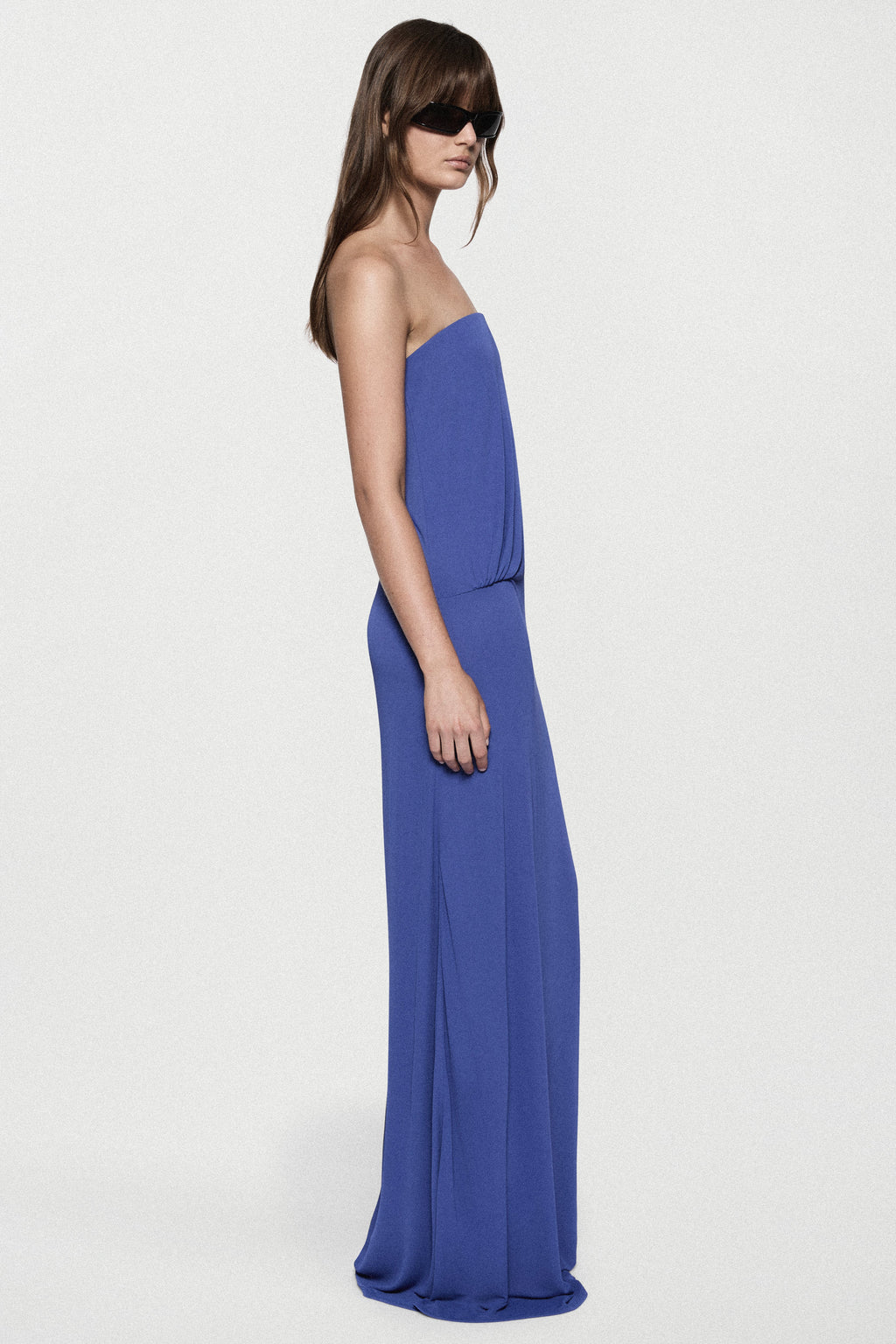 Blue strapless jersey maxi dress with straight column silhouette and side drape.