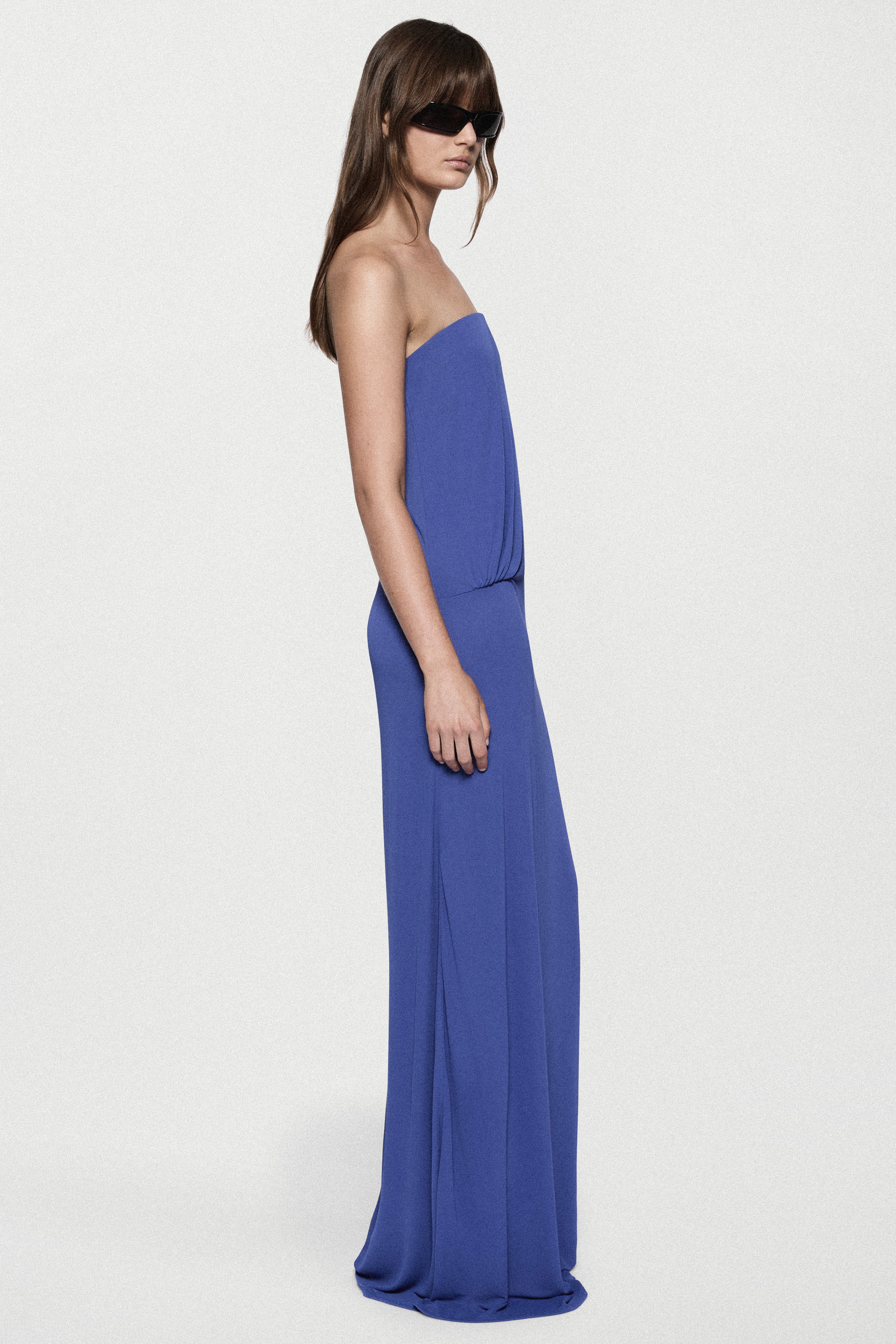 Blue strapless jersey maxi dress with straight column silhouette and side drape.