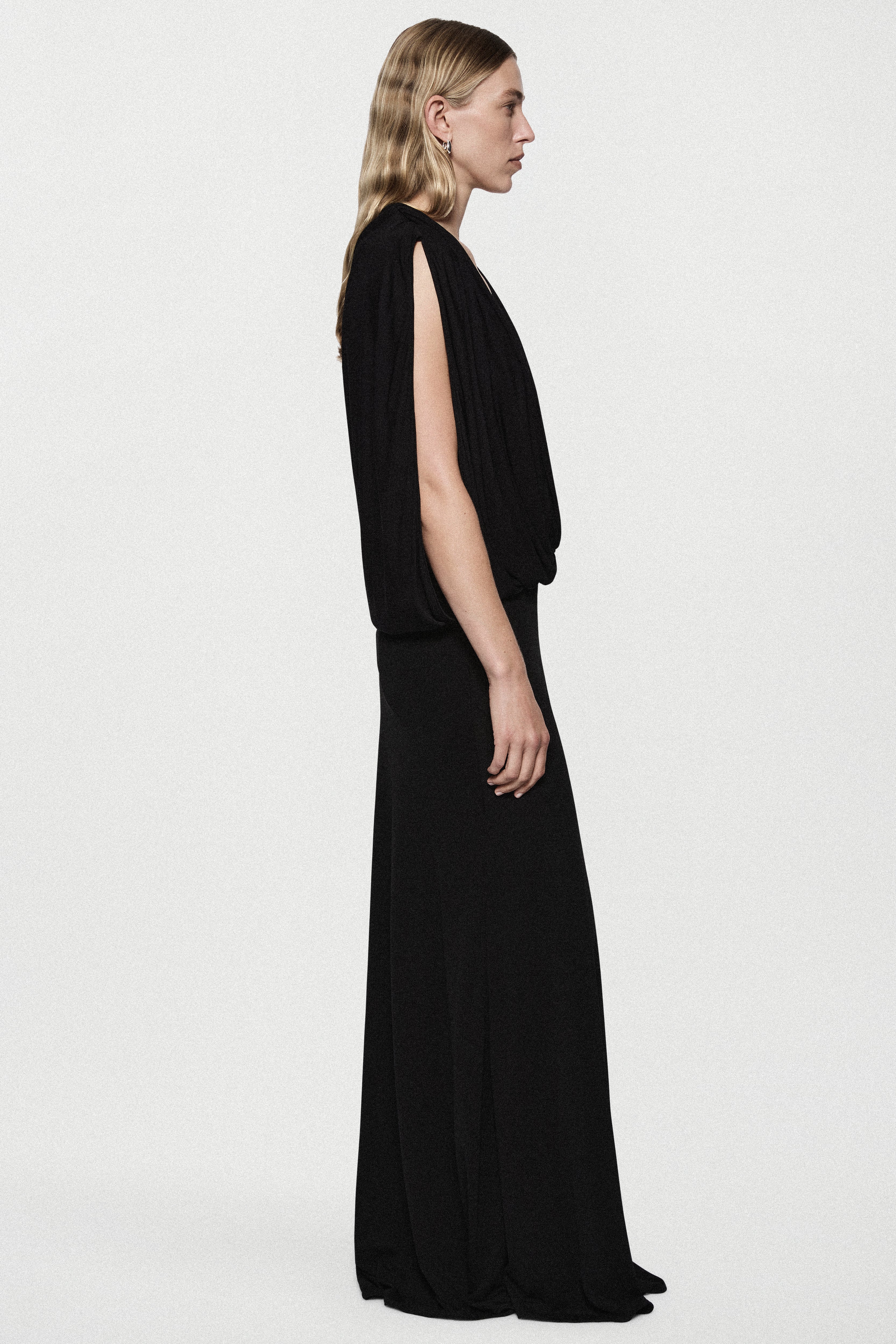 Black sleeveless jersey cowl gown in side view with draped V neckline and long hem