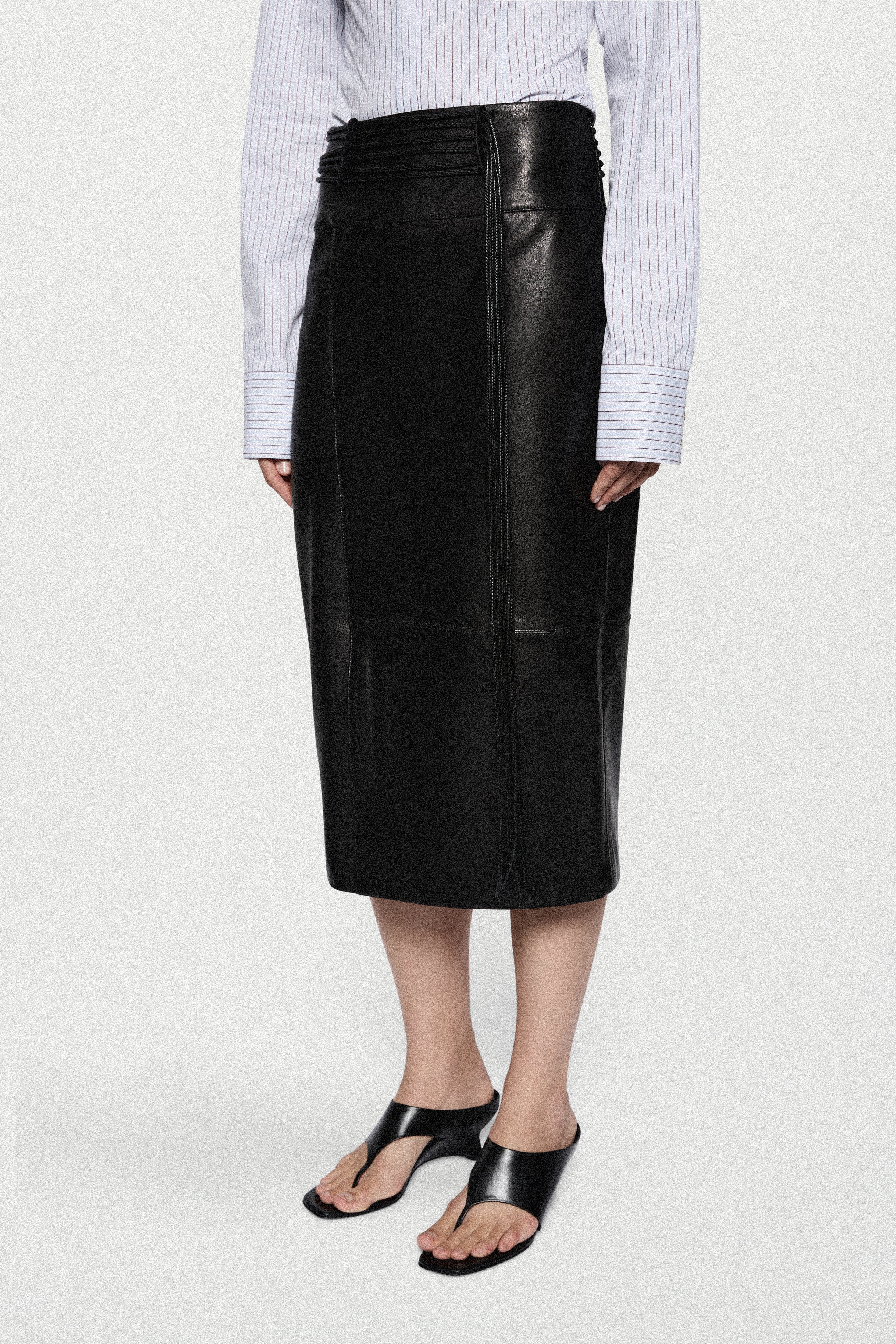 Black leather midi skirt with high waist, center seam, and smooth glossy finish