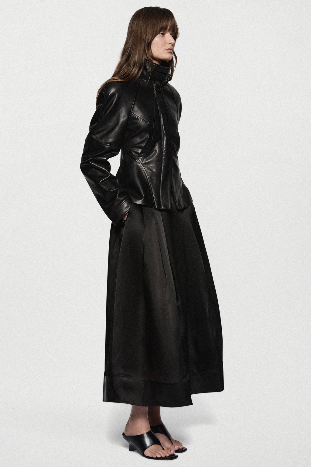 Black leather jacket side view with stand collar, front zip, and flared peplum.