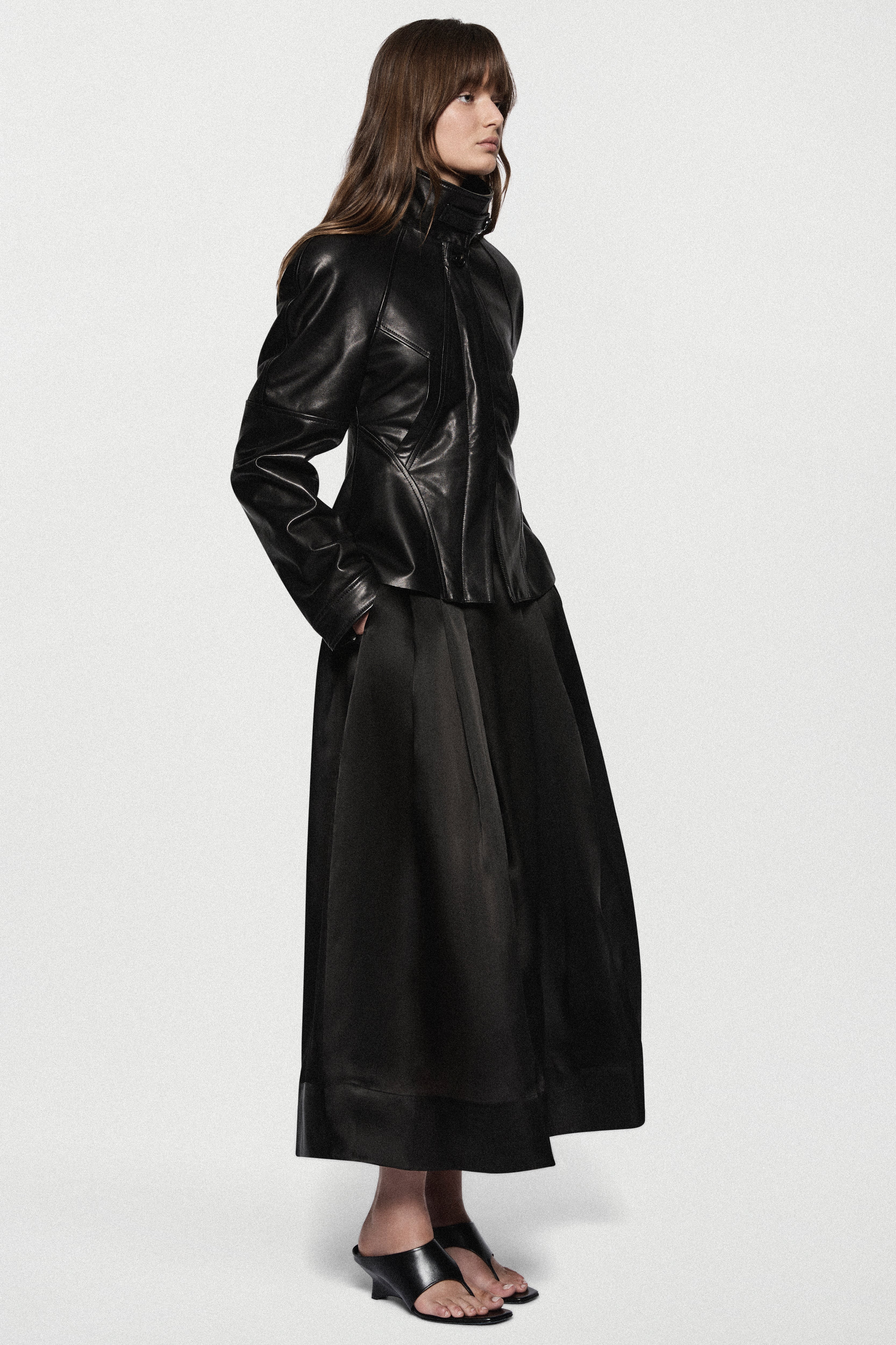 Black leather jacket side view with stand collar, front zip, and flared peplum.