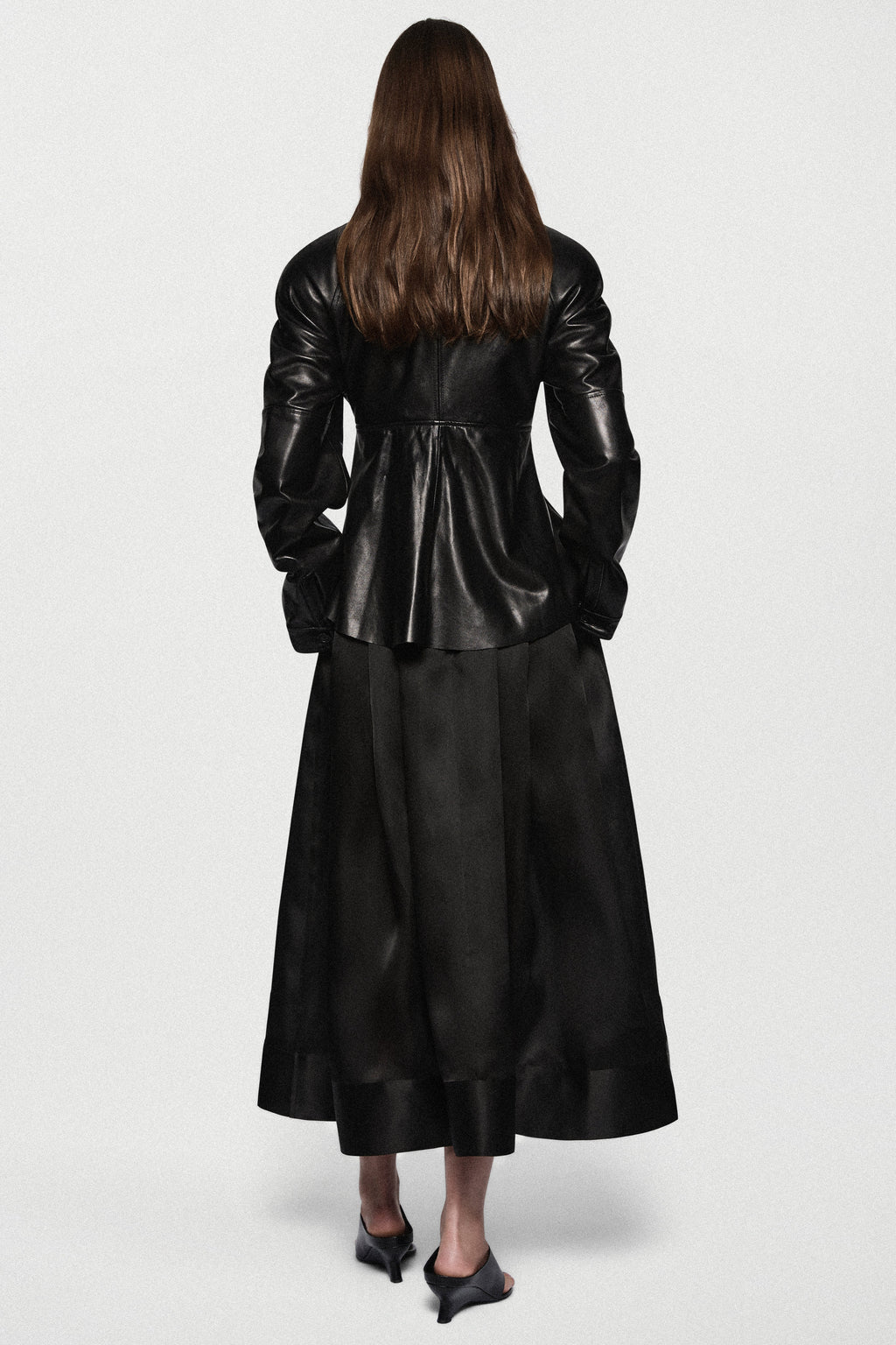 Black leather jacket back view with stand collar, central seam, and flared peplum hem.