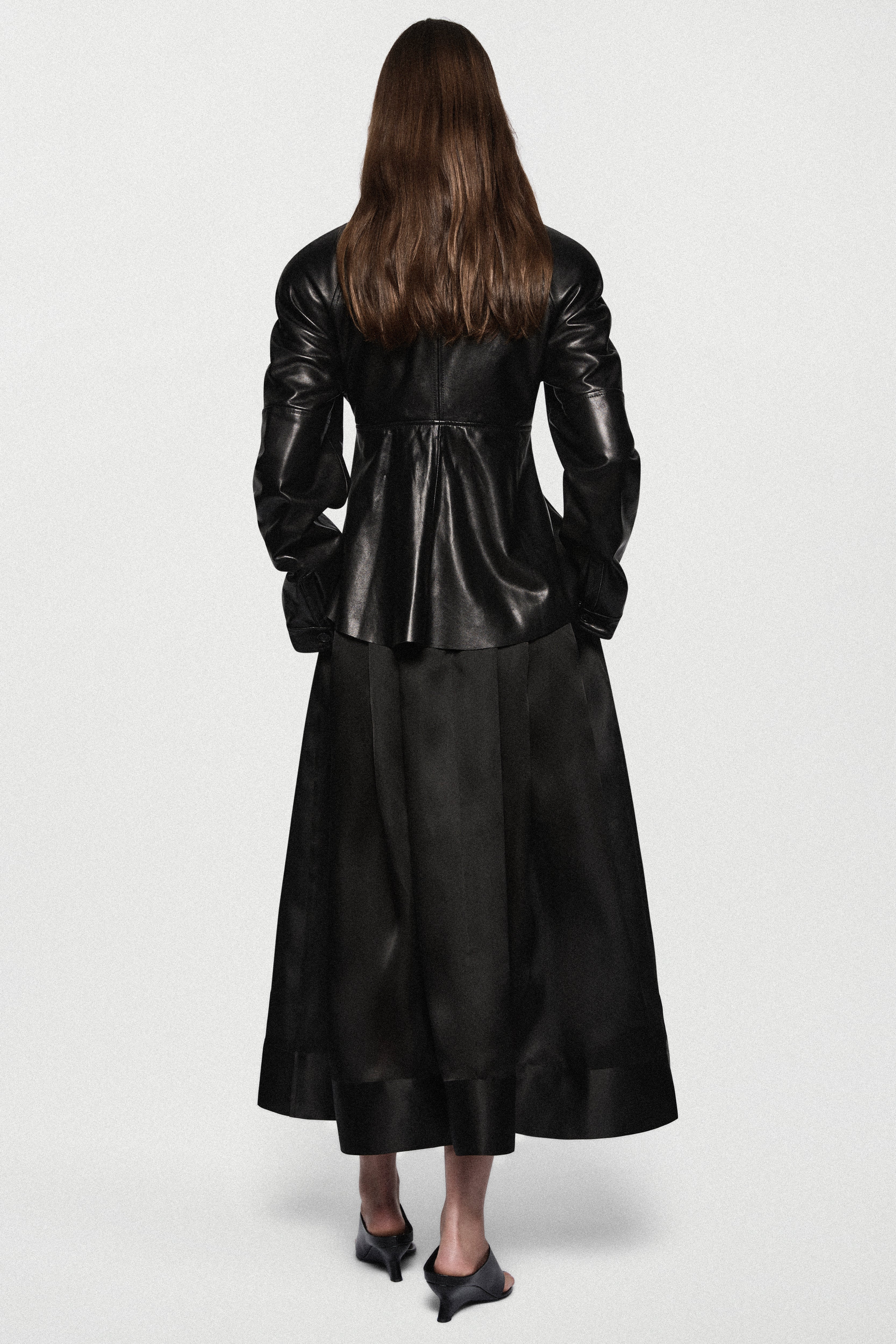 Black leather jacket back view with stand collar, central seam, and flared peplum hem.