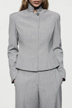Grey tailored jacket close-up with high neck, button front, and structured seams.