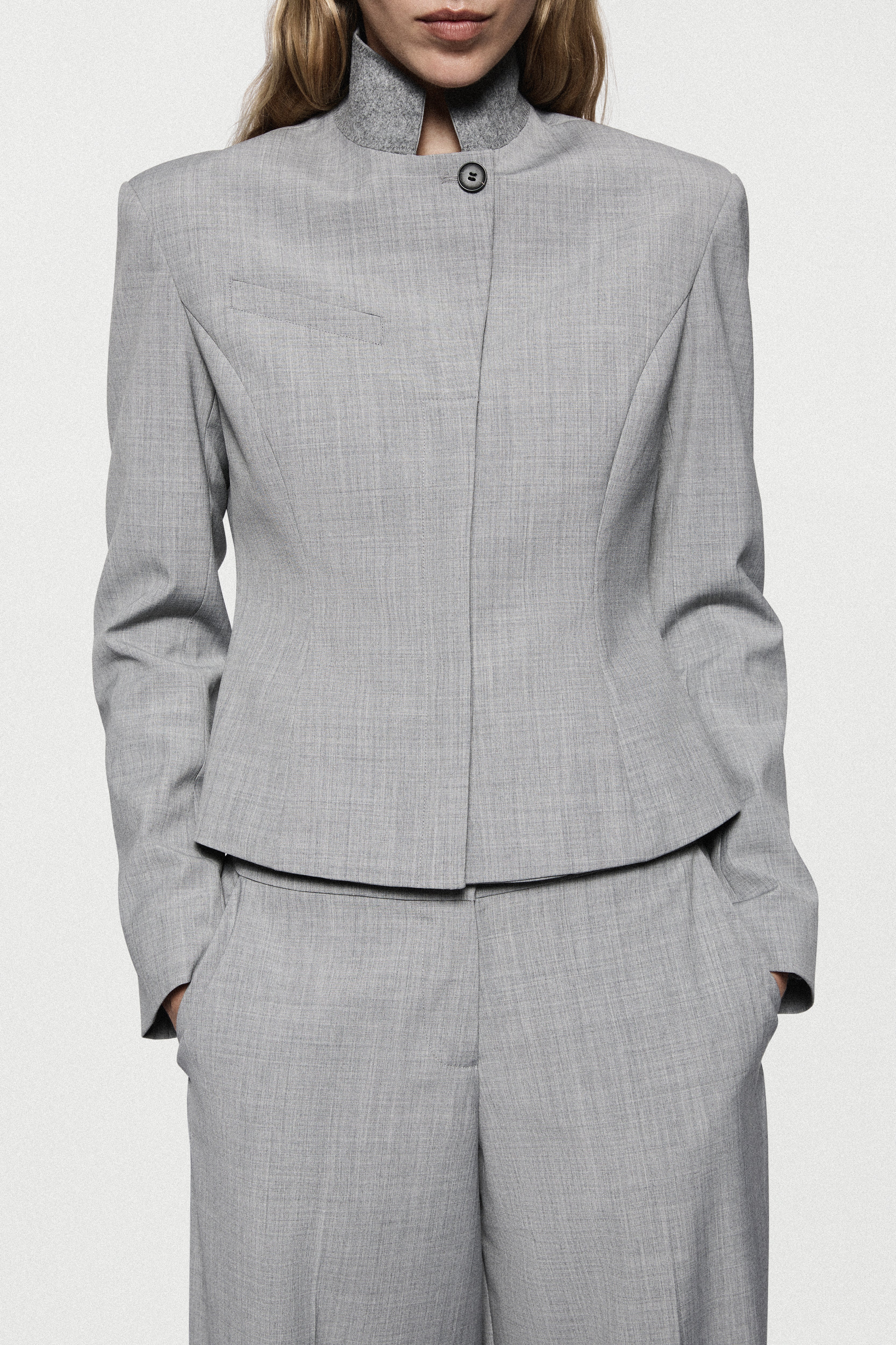 Grey tailored jacket close-up with high neck, button front, and structured seams.