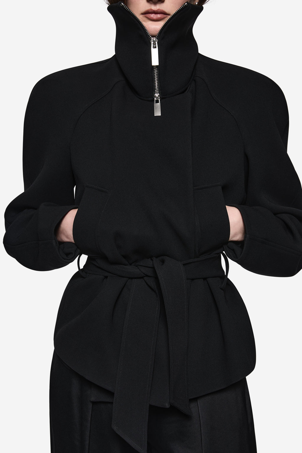 Black acetate jacket close-up: stand collar with silver zip pull and tied waist peplum.