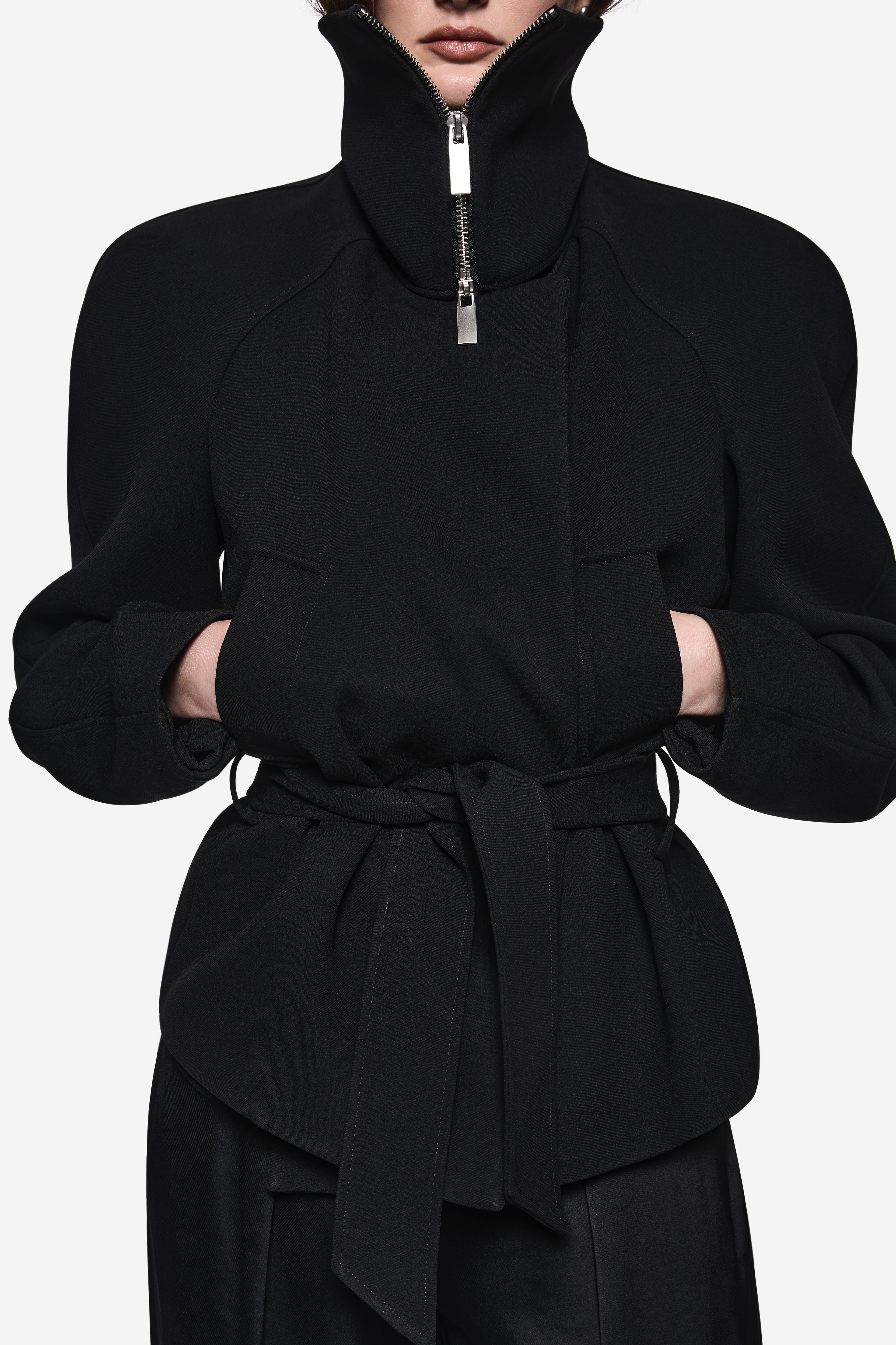 Black acetate jacket close-up: stand collar with silver zip pull and tied waist peplum.