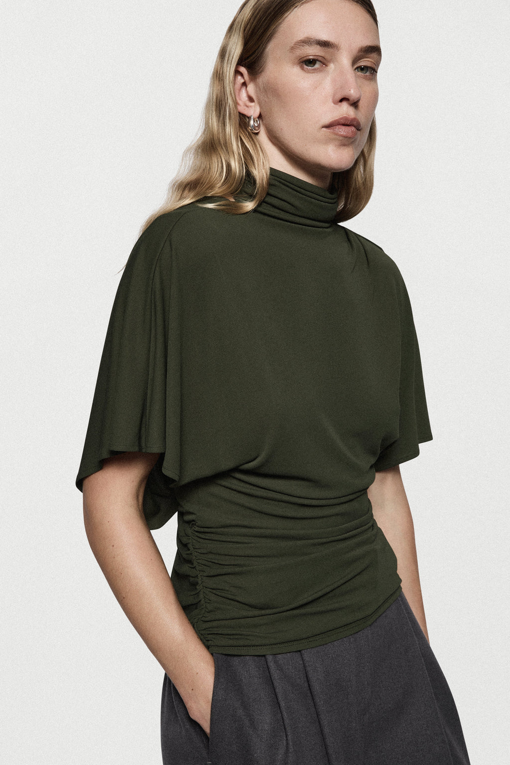 Hunter green cape jersey turtleneck top with short sleeves and draped waist gathers.