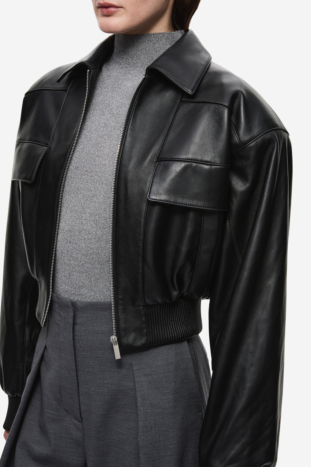 Black leather aviator jacket close-up with snap flap shoulder pockets and zip